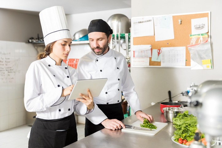 Cooks Using Tablet Computer In Restaurant Kitchen