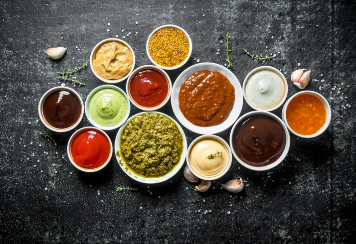 Pesto sauce, guacomole, ketchup, mustard, barbecue sauce in bowls.