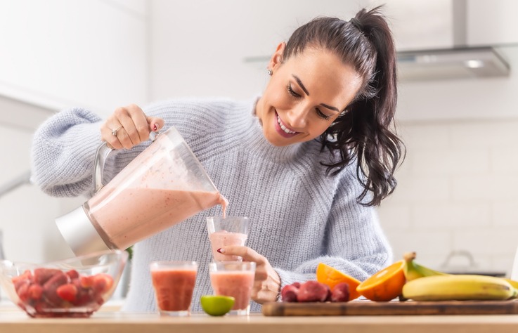 Woman pours fruit smoothie into cups in a kitchen.