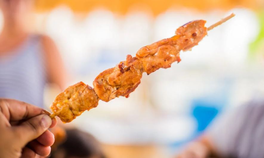 A guy holding a chicken skewer